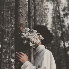 a man standing next to a tree with white flowers in his hair and wearing a black hat