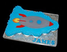 a cake shaped like a rocket ship with the name james written in blue frosting