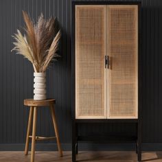 a tall wooden cabinet sitting next to a vase filled with dry grass on top of a hard wood floor