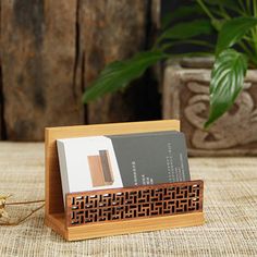 a wooden business card holder with two credit cards in it on a table next to a potted plant