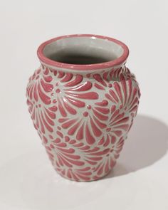 a red and white vase sitting on top of a table next to a white wall