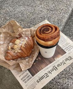 a cup of coffee next to a pastry on top of a newspaper