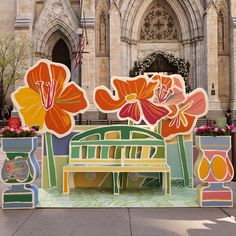 an artistic display in front of a large building with flowers on the wall and bench