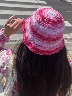 a woman wearing a pink and white hat on top of her head next to a street