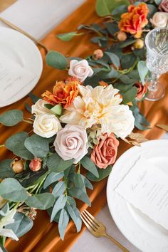 the table is set with white plates, silverware and colorful flowers on top of it