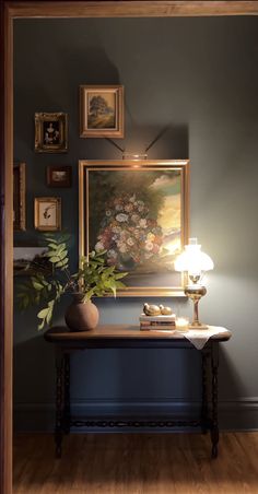 a painting is hanging on the wall next to a table with a lamp and flowers