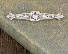 This vintage pin has a nice slender design. Although the brooch isn't very tall it is 2.75 inches long. Beautiful european cut diamonds and trillion cut blue sapphires add color and sparkle to this vintage pin. It has carefully carved filigree and milgrain. Normal price: $2,995.00 Special Internet Price: $2,250.00 Metal Type: 14k White Gold Gemstones: Diamonds Sapphire Gemstone Shape: European, Trillion Diamonds: H-I color, Si1 clarity, 0.50tdw total diamond weight Sapphires: Blue Sapphire, 0.10 Vintage Blue Diamond Brooch, Vintage Blue Diamond Brooches, Trillion Diamonds, Wedding Brooch, European Cut Diamonds, Sapphire Gemstone, Vintage Pins, Rhodium Plated, Types Of Metal