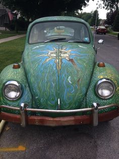 an old beetle painted with blue and green designs on it's front bumper is parked in a parking lot