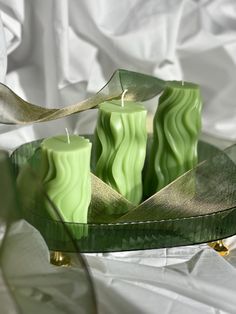 some green candles are sitting on a plate with gold trimmings and ribbon around them