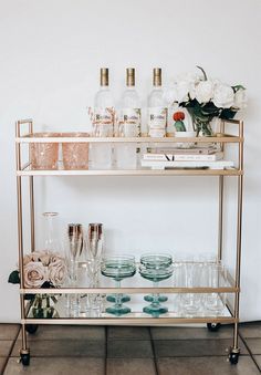 a gold bar cart with glasses and bottles on the top, flowers in vases next to it