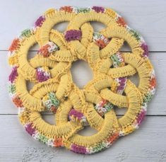 a crocheted doily is shown on a white wooden surface, with multicolored flowers in the center