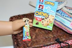 a toy hand holding a cereal bar next to a box of chewy