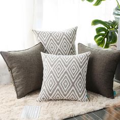 three pillows on a rug next to a computer keyboard and potted plant in front of a window