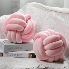 two pink pillows sitting on top of a white bed next to a stack of books