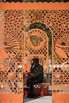 a man sitting on top of a wooden bench under an orange gate with intricate designs