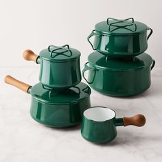 three green pots with wooden spoons on a marble countertop, one has a lid and the other has a handle