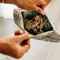 a woman holding an old photo in her wedding dress while another person holds it open