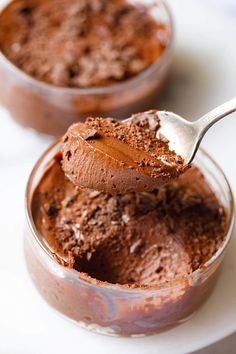 two bowls filled with chocolate pudding on top of a white plate and one has a spoon in it