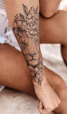 a woman's arm with a lion and flowers tattoo on her left leg, while she is sitting down