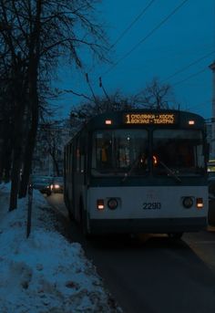 a bus is driving down the street in the snow at night with its lights on