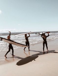 three surfers carrying their boards on the beach