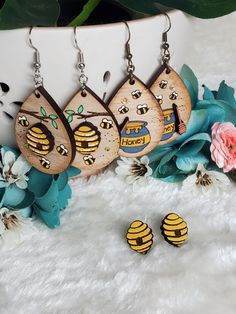 three wooden earrings with bees on them next to flowers