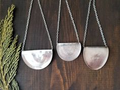 three pieces of metal hanging from chains on a wooden table next to a pine branch