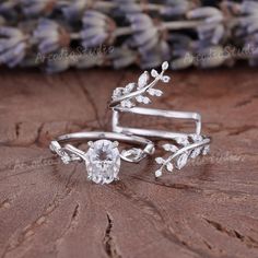 two pieces of silver jewelry sitting on top of a piece of wood with flowers and leaves