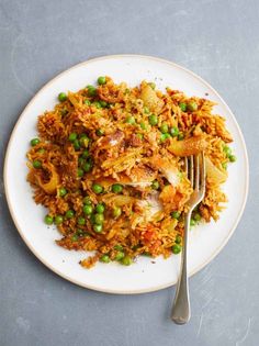 a white plate topped with rice and peas next to a fork on a gray surface