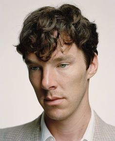 a close up of a person wearing a suit and tie with curly hair looking at the camera