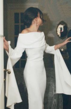 a woman in a white dress standing next to a door