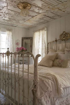 a white bed sitting in a bedroom next to a window with curtains and pillows on top of it