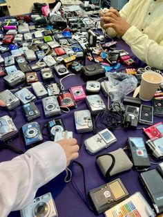 two men sitting at a table covered with cell phones and other electronic gadgets