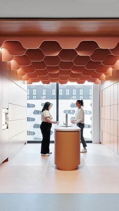 two women are standing in an office with white walls and wooden ceilinging, while one woman is talking on the phone