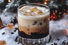 a glass filled with liquid and ice on top of snow covered ground next to christmas decorations