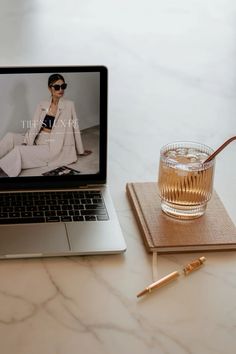 a laptop computer sitting on top of a table next to a glass filled with liquid