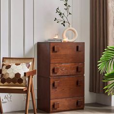 a wooden chest of drawers next to a chair and potted plant in a room