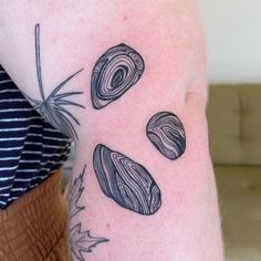 a woman's arm with three rocks and leaves tattoo on the left side of her body