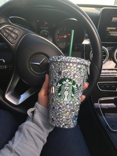 a person holding a starbucks cup in their hand while sitting in the driver's seat of a car