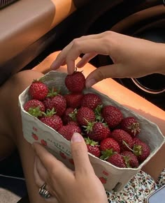 a woman is holding a box full of strawberries