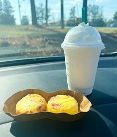 two muffins and a drink in a paper cup on the dashboard of a car