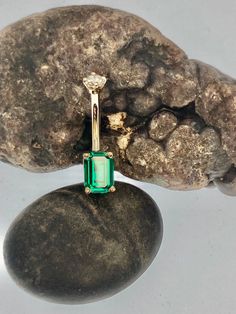 an emerald colored ring sitting on top of a rock next to a large rock with two smaller rocks in the background