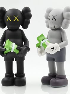 two black and white figurines with yellow crosses on their faces, one holding a green box