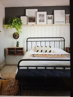 a bedroom with white walls and black iron bed frame, pillows and pictures on the wall