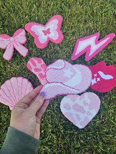 someone is holding up pink felt hearts and seashells in the grass with butterflies on them