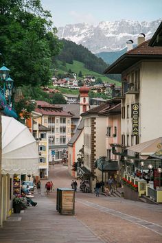 people are walking down the street in front of buildings with mountains in the back ground