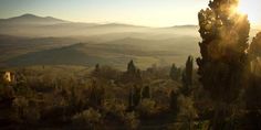 the sun shines brightly over rolling hills and trees in the foreground, with mountains in the distance