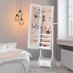 a white jewelry cabinet sitting next to a bed