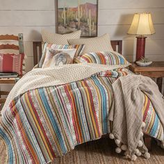 a bed with colorful striped comforter and pillows in a room next to a chair