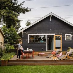 a woman standing on top of a wooden deck in front of a blue house with lawn chairs